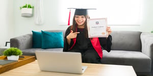 Woman in cap and gown graduating over computer in 2020