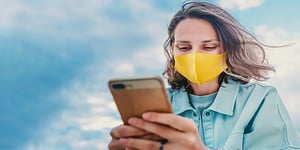 Woman smiling wearing yellow mask looking at her phone for networking