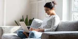 Woman sitting on couch crossing her legs on her laptop smiling