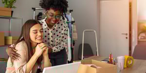 Two women at a desk smiling at white laptop in office