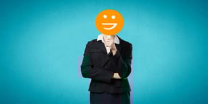 Woman in suit holding an orange smiling face sign over her face on top of blue background