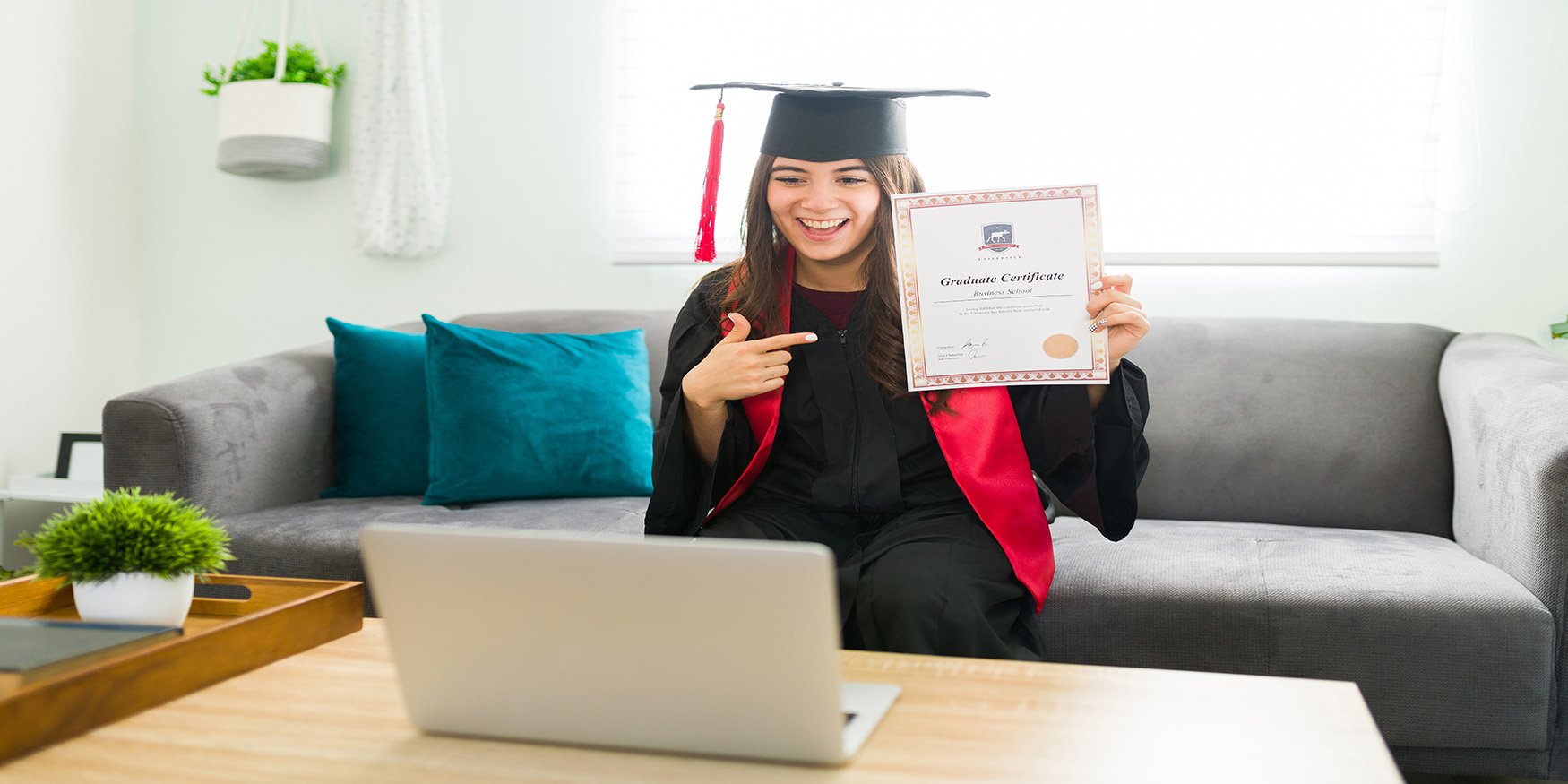 Woman in cap and gown graduating over computer in 2020