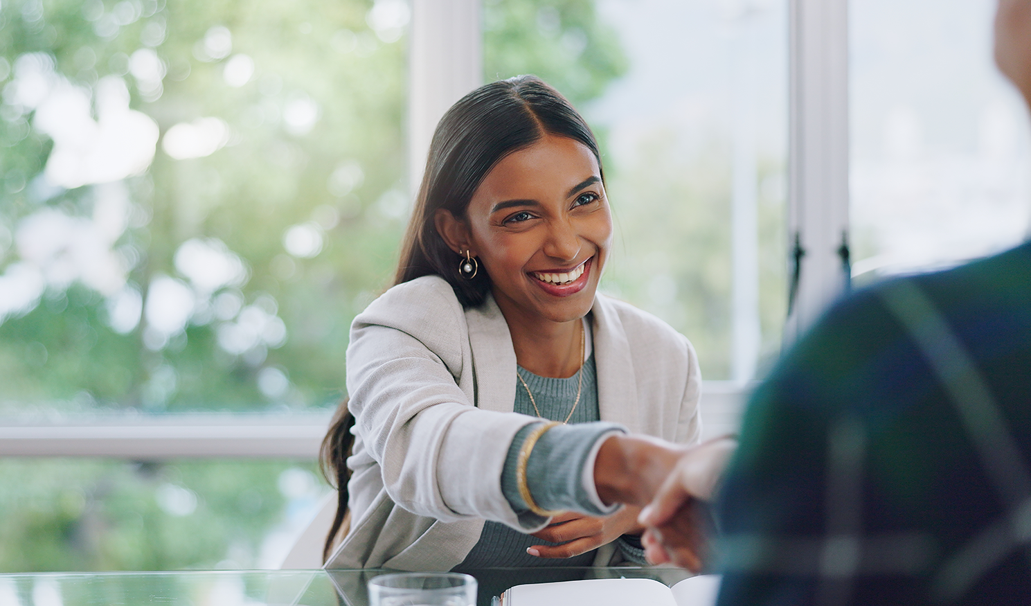 Woman smiling and shaking hands layered on top of window background.